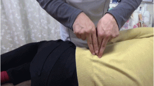 腰の筋肉の隙間に深く指を差し込みほぐす指圧