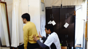 親指で骨盤と腰の間を押さえてイスから立ち上がる動作を補助するように腰仙関節の添えた親指で身体全体を誘導します